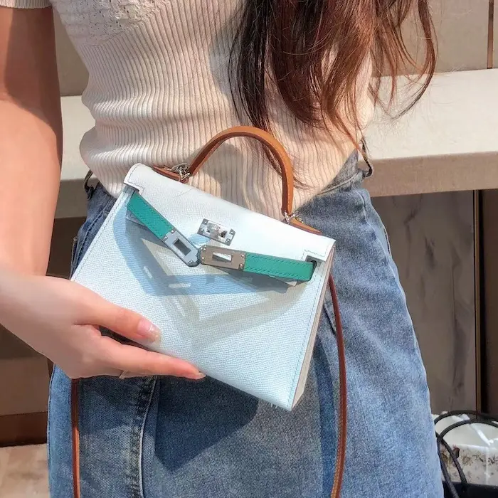 Side view of model holding blue Epsom replica Kelly 19cm bag near waterfront