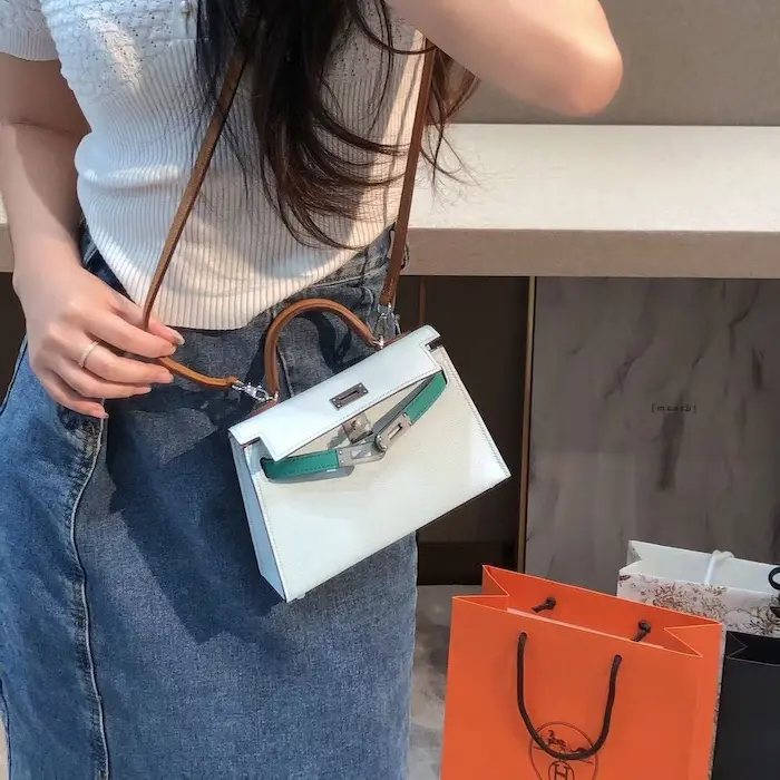 Model posing with replica blue Kelly 19cm bag against urban architecture backdrop