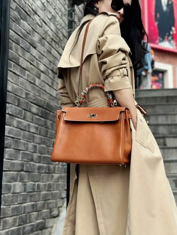 Woman wearing replica Hermes Kelly 32cm Gold bag with shoulder strap in city streets