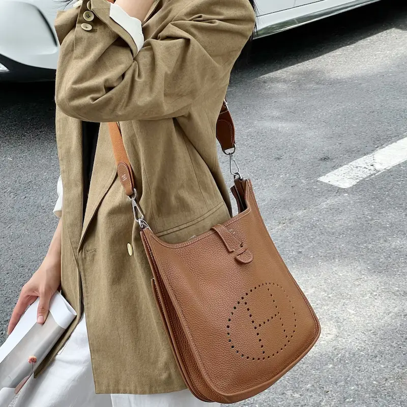 Woman carrying Gold Clemence leather replica Hermes Evelyne 29 crossbody bag in city