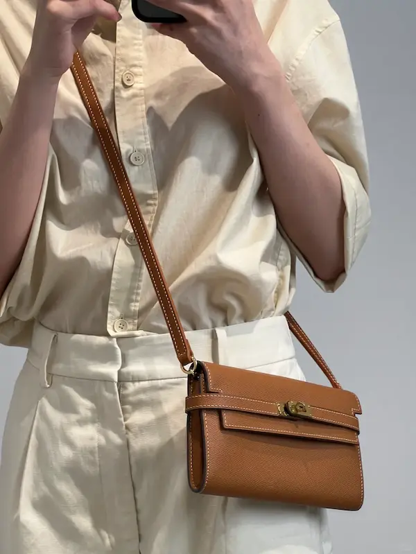 Model wearing gold replica Hermes Kelly as crossbody bag with casual outfit