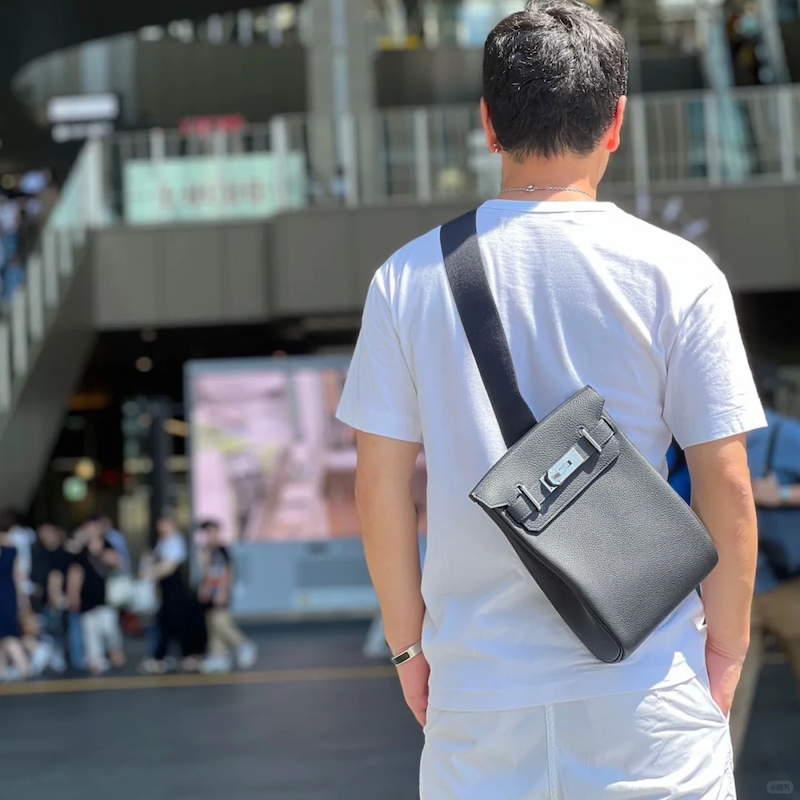 Man styling black Replica Hermes HAC à Dos backpack in urban setting
