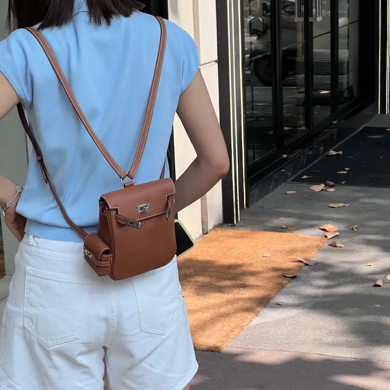 Woman styling a Gold Brown Replica Hermes Kelly Jump Backpack in a city setting